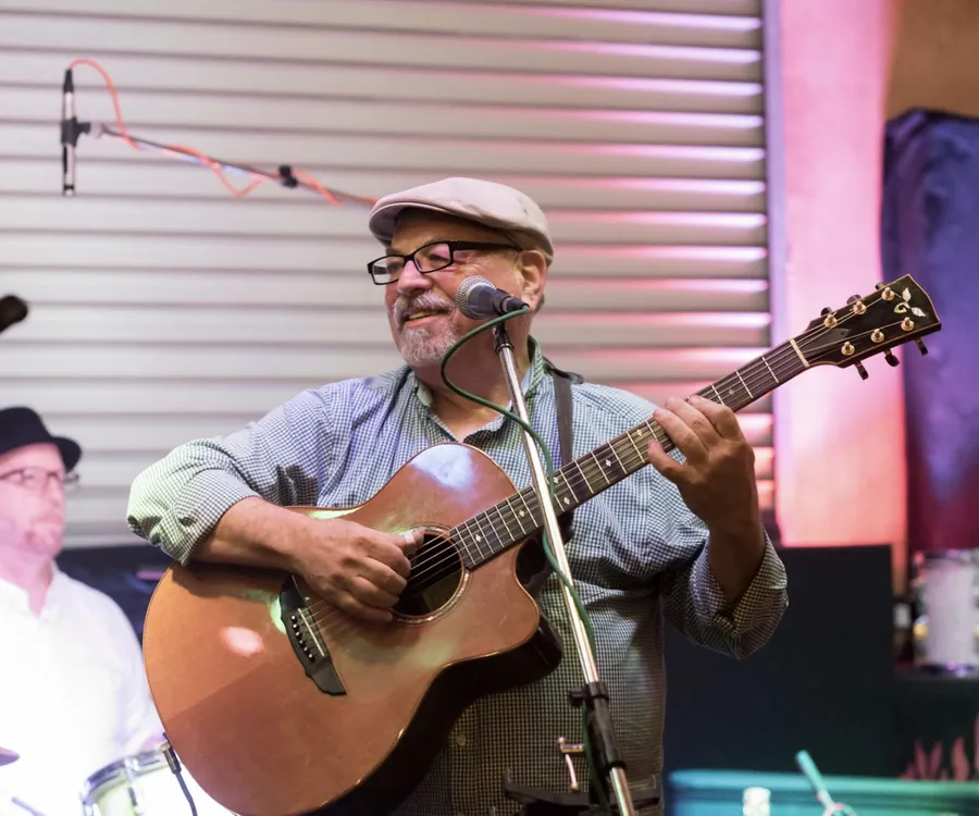 Ron performing at a microphone with an acoustic guitar