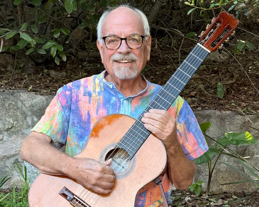 Ron smiling outdoors with a classical guitar